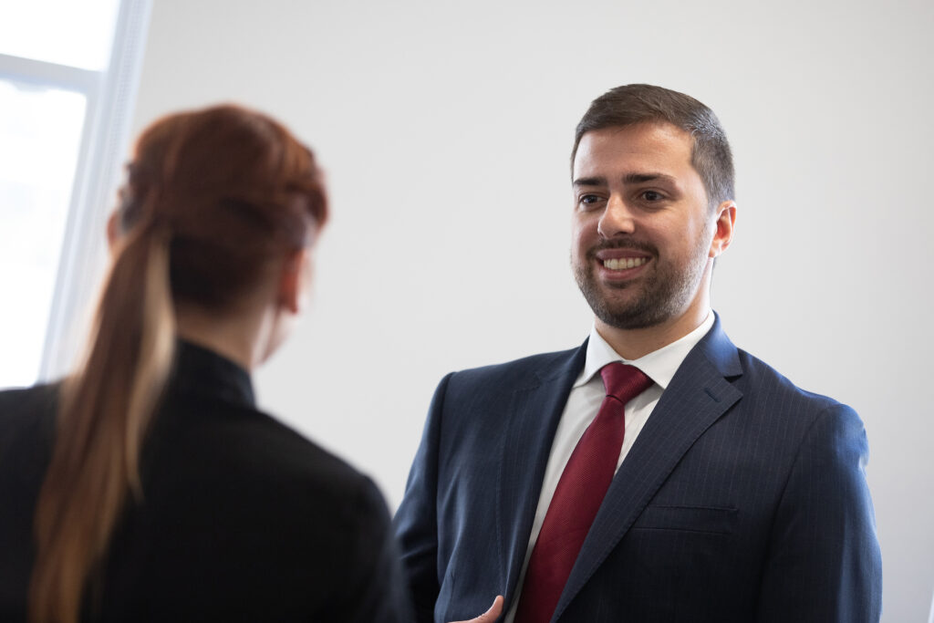 Man in a suit and tie standing in front of a woman smiling in conversation