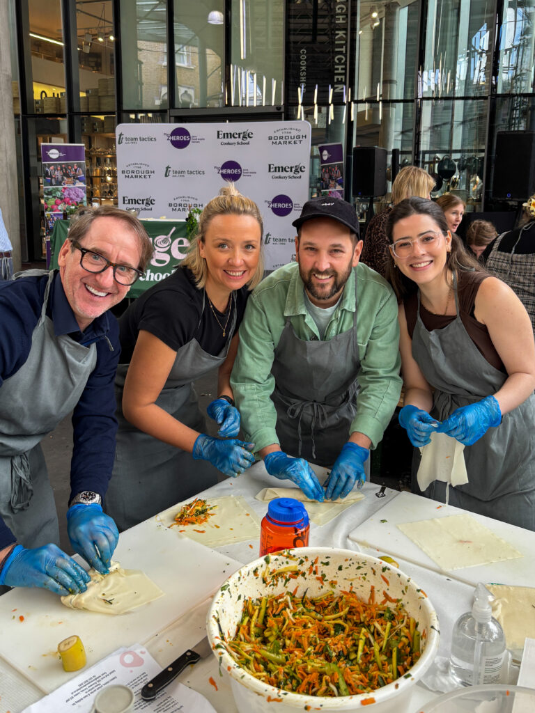 Four people smiling, looking at camera whilst cooking
